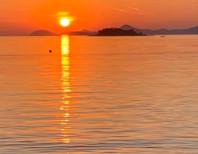 View from ferry at sunset approaching Dubrovnik coastline.