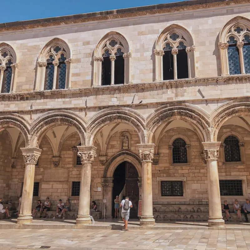 People seated by the Rector's Palace entrance beside carved pillars.