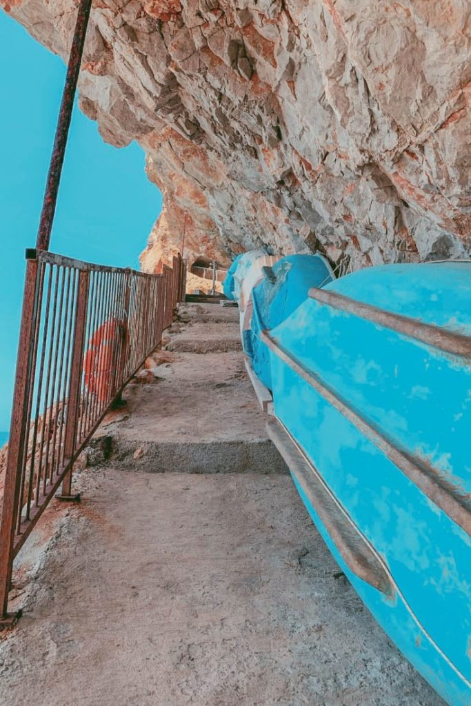 Narrow pathway carved into the cliffs leads down to Pasjača Beach. Little boats are stored under the cliffs.