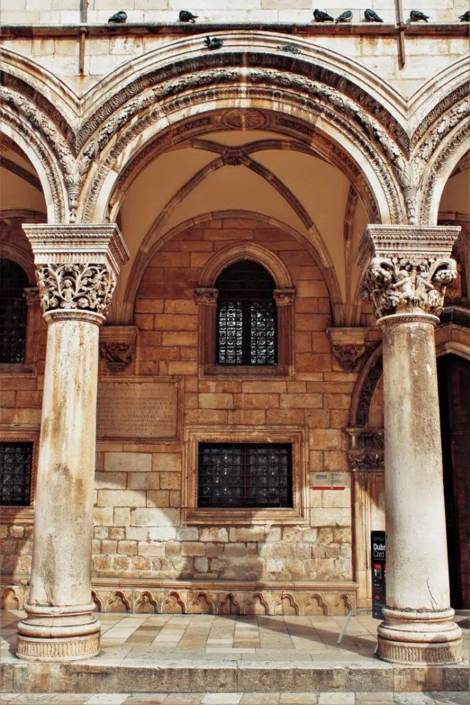 Image shows carved columns of the entrance to the Rector's Palace. It houses the cultural and historical department of the Dubrovnik Museums, where portraits of famous Dubrovnik residents (Getaldić, Gundulić, Bošković, among others), keys to the city gates, objects from the old city pharmacy Domus Christi, etc. are exhibited